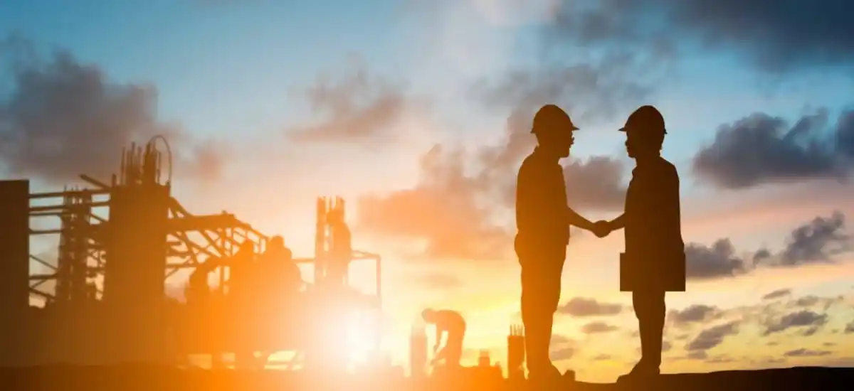 twee personen met bouwhelmen schudden elkaar de hand bij zonsopkomst| DID-online.nl